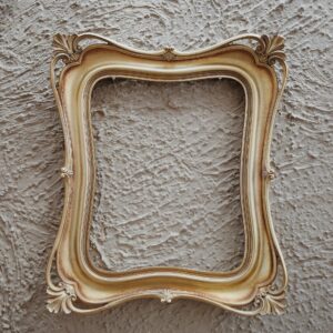 Antique golden frame with ornate details against a textured gray wall, perfect for art and design themes.