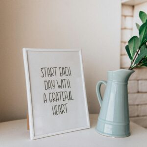 Framed quote 'Start each day with a grateful heart' next to a vase indoors.