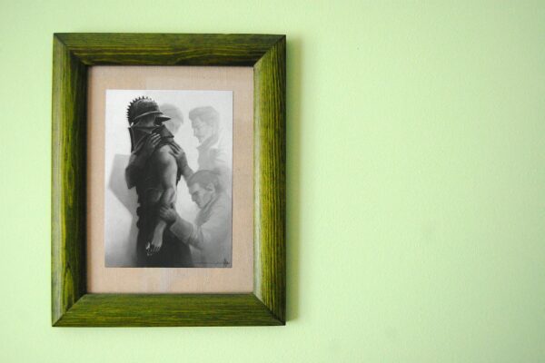Green wooden frame holding a grayscale art print on a soft green wall.