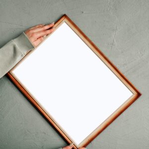 A blank wooden frame held by hands against a grey concrete wall, perfect for mockups.