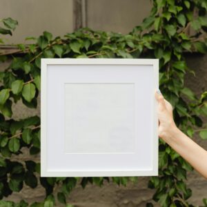 Empty white frame held by hand with lush green ivy backdrop.