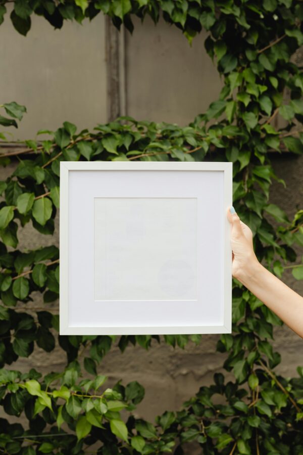 Empty white frame held by hand with lush green ivy backdrop.